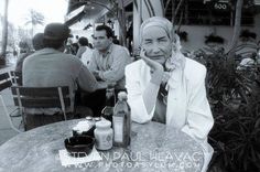 black and white photograph of man sitting at table in outdoor cafe with bottles on the table