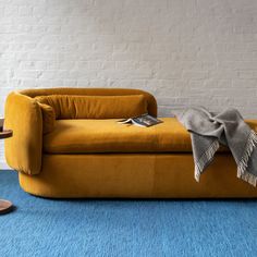 a yellow couch sitting on top of a blue carpet next to a white brick wall