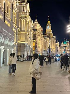 people are walking down the street in front of large buildings at night with lights on