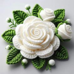 a crocheted white rose with green leaves