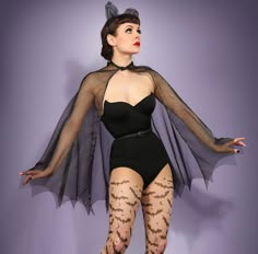 a woman in a black bodysuit with sheer sleeves and fishnet stockings, posing for the camera