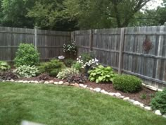 a garden with lots of plants and rocks in the grass next to a wooden fence