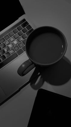 a cup of coffee sitting on top of a laptop computer next to it's keyboard