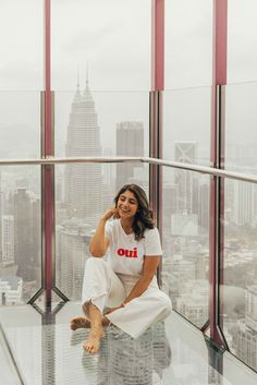 a woman sitting on top of a glass floor in front of a cityscape