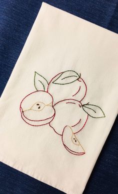 an embroidered piece of cloth with apples and leaves on it, sitting on a blue surface