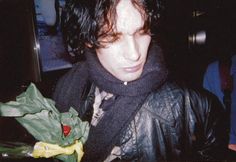 a young man in a leather jacket holding a flower