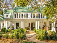 a white house with black shutters on the front and green roof, surrounded by trees