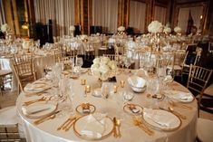 the tables are set with white flowers and gold place settings for an elegant wedding reception