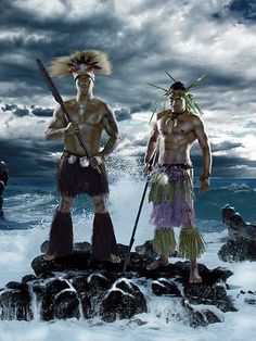 two native american men standing on rocks in the ocean