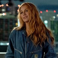 a woman with long hair standing in front of a cityscape and looking off into the distance