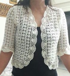 a woman is wearing a white crocheted cardigan and black dress with her hands in her pockets