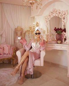 a woman sitting on a chair in front of a dressing table with a mirror and chandelier