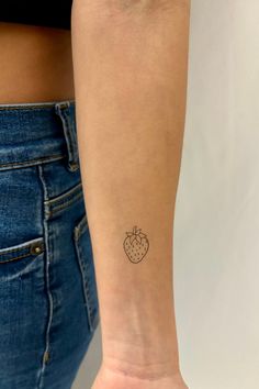 a small strawberry tattoo on the left inner forearm and wristband is shown in front of a woman's right arm