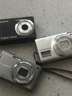 three cameras sitting on the ground next to each other, one is silver and the other is black