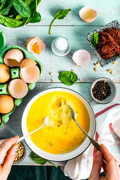 two hands holding a spoon over a bowl of soup with eggs and spinach on the side