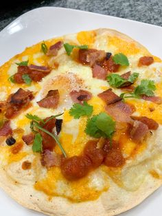 a pizza with bacon, cheese and cilantro on it sitting on a white plate