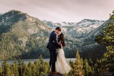 a bride and groom standing on top of a rock in front of the mountain range