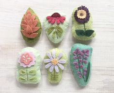 six felt flowers and leaves are arranged on a table