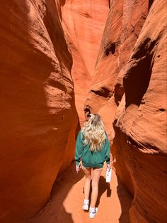 a woman in green shirt and white shoes walking through an area with red rock formations