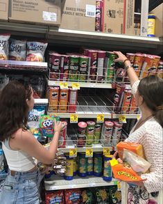 two women are shopping in a store with canned food on the shelves and one is pointing at something