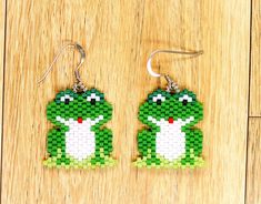 a pair of green and white beaded frog earrings sitting on top of a wooden table