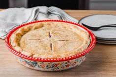 a pie sitting in a bowl on top of a wooden table next to two plates