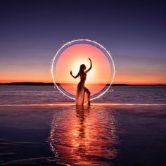 a woman is standing in the water with her arms up and holding a circular object above her head