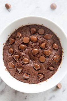 a white bowl filled with chocolate pudding and topped with a gold spoon, on top of a marble surface