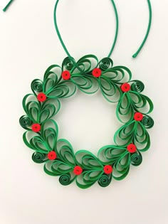 an origami christmas wreath with red buttons and green string hanging on a white wall