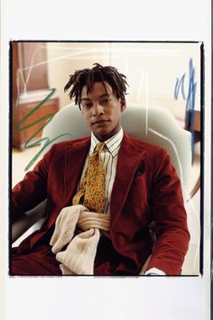 a man with dreadlocks sitting in a chair wearing a red suit and yellow tie