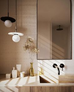 a bathroom sink sitting under a mirror next to a vase filled with flowers and two lights