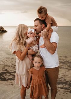 a man, woman and two children standing on the beach with their arms around each other