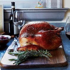 a whole turkey sitting on a cutting board next to wine glasses