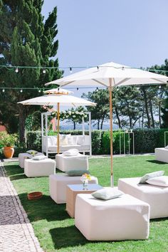 an outdoor seating area with umbrellas and white couches on the grass near trees