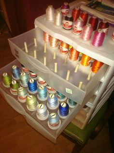 an assortment of spools of thread in a storage bin on top of a refrigerator