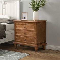 a bedroom scene with focus on the nightstand and bed in the foreground, along with a potted plant