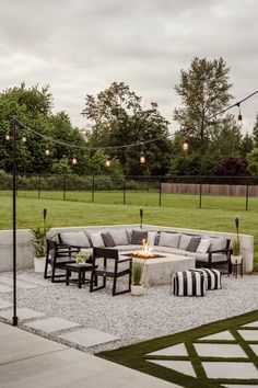 a fire pit surrounded by black and white furniture in the middle of a grassy area