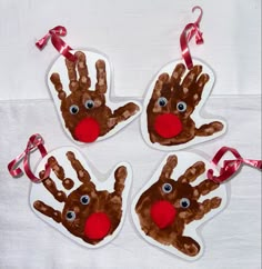 four handprinted christmas ornament hanging on a white table with red ribbon