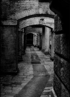 black and white photograph of an alleyway with brick walls, arched doorways and cobblestones