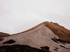 the top of a mountain covered in brown and white snow on a cloudy sky day