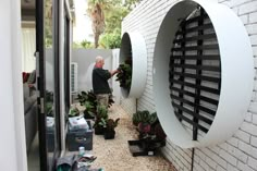 a man standing next to a white brick wall with plants growing out of the window