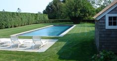 a backyard with a swimming pool and lawn furniture in the foreground, surrounded by hedges