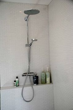 the shower head is open and there are soaps on the shelf next to it