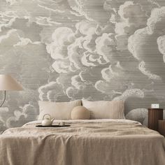 a bed sitting under a lamp next to a wallpaper covered in cloud like designs