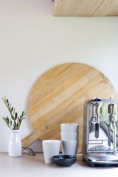 the coffee maker is next to cups and a cutting board on top of a counter