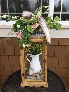 a vase filled with flowers and greenery on top of a small table next to a window