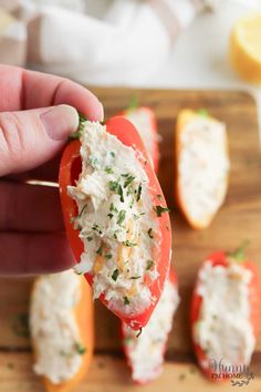 a person is holding up a piece of crab salad on a wooden cutting board with oranges and lemons in the background