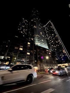 cars are driving down the street in front of tall buildings at night with lights on