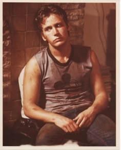 a young man sitting in front of a brick wall with his hands on his knees