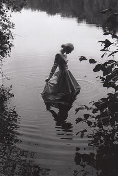 a woman is standing in the water wearing a dress and holding a bag with her hands